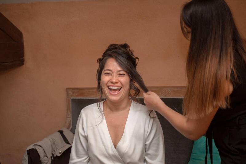 coiffeuse qui texturise les mèches ondulés devant le visage de la mariée lors de son mariage au château de Talancé à Denice